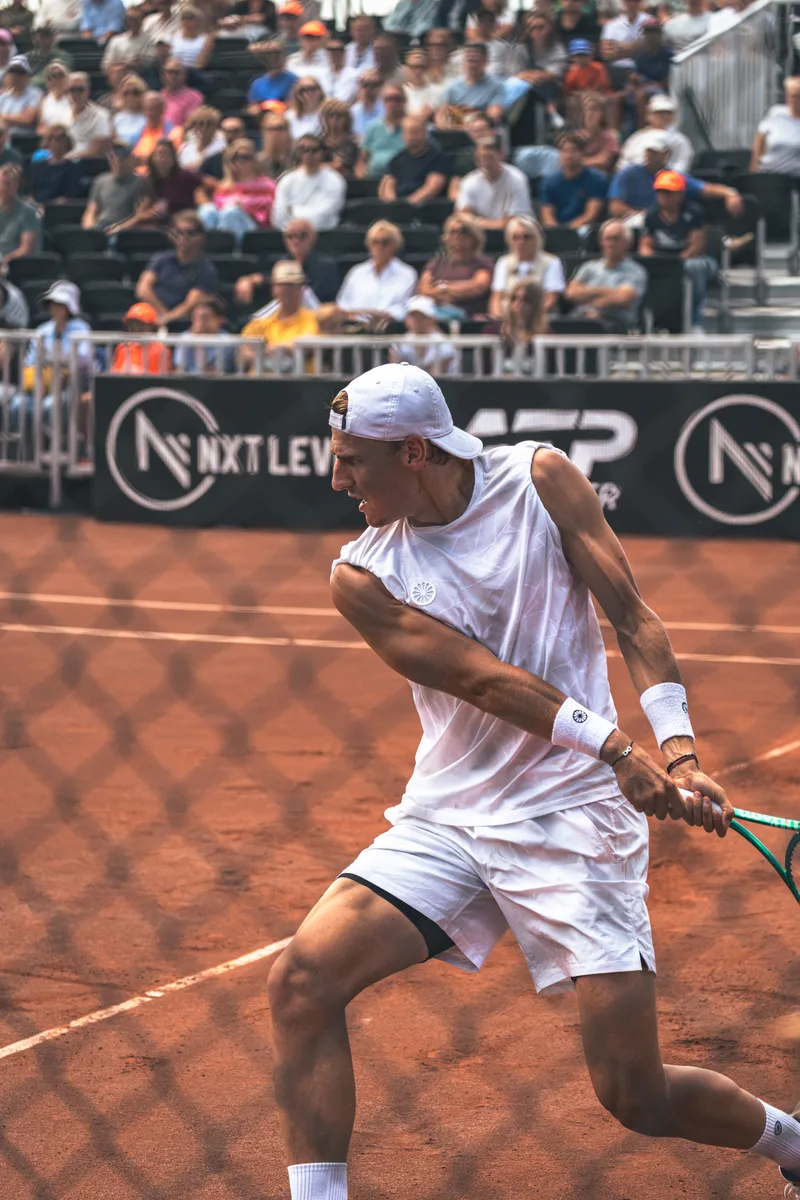 Backhand langs de lijn met het hek en de tribune op de achtergrond