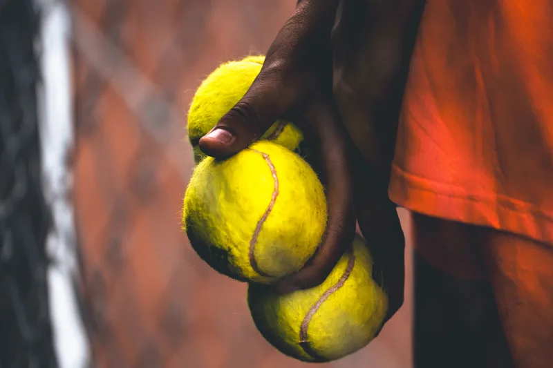Hand van een ballenkind met twee tennisballen voor een oranje shirt