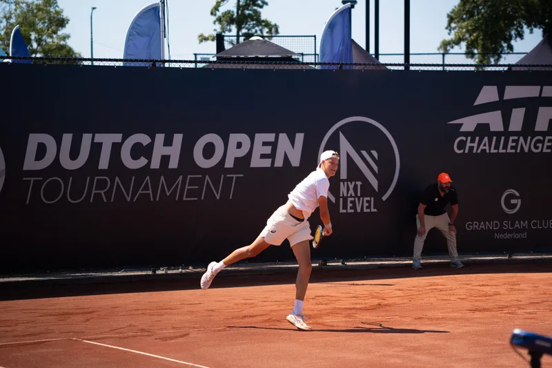Speler loopt uit na de service op de gravelbaan van het Dutch Open