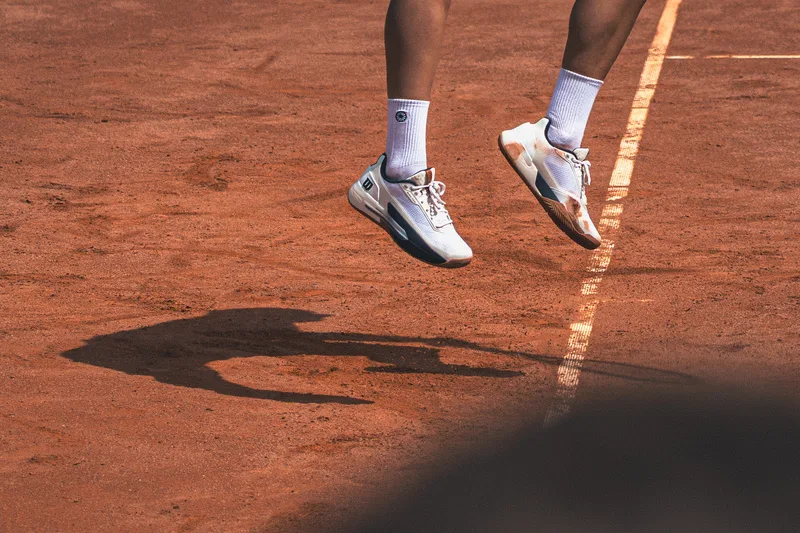 Detail van tennisschoenen en de schaduw van de speler op het gravel